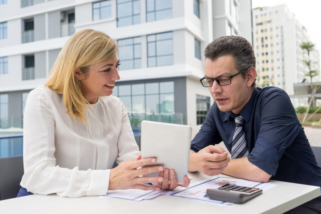 smiling woman showing male colleague tablet screen in cafe